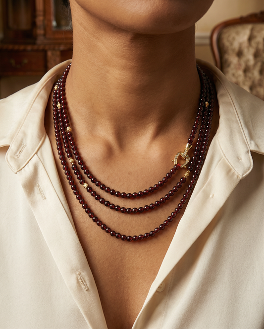 Person wearing a triple-strand dark red beaded necklace with gold accents and clasp, paired with a cream shirt
