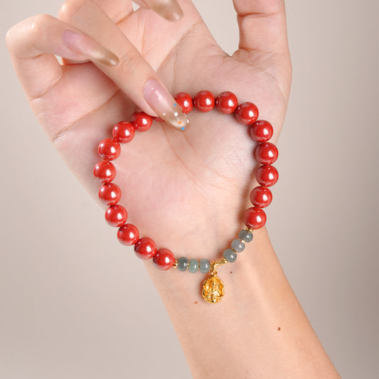 Hand holding red beaded bracelet with gray beads and gold charm on beige background
