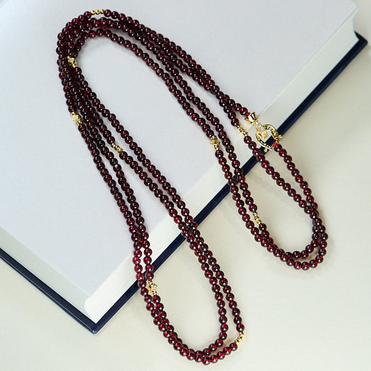 Long garnet bead necklace with gold accents and decorative clasp on a white book